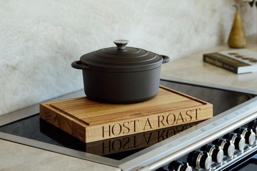 Black cast iron pot on a wooden trivet with 'HOST A ROAST' text on a stove.