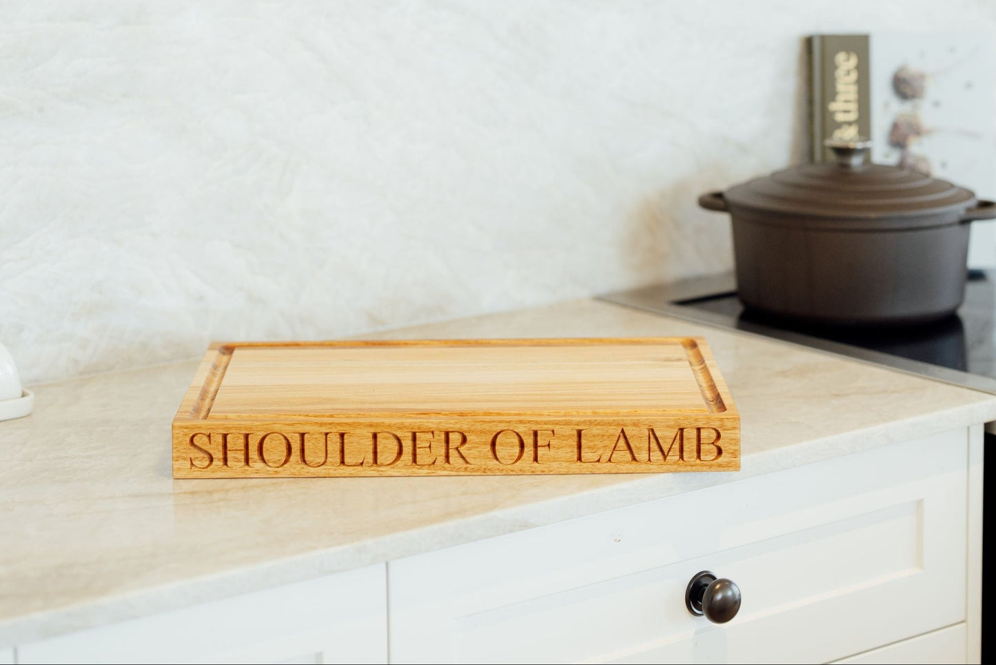 Wooden cutting board with 'SHOULDER OF LAMB' engraving on a kitchen counter.