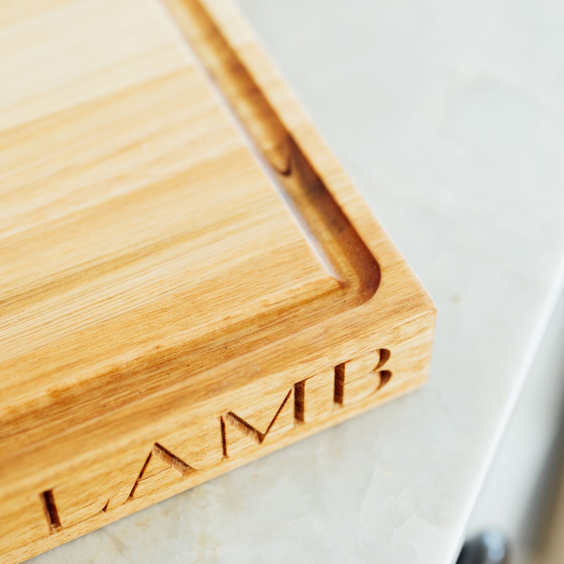 Wooden cutting board with 'LAMB' engraving on a marble surface